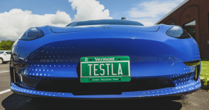 The front of a blue Tesla car with the license plate "TESTLA"